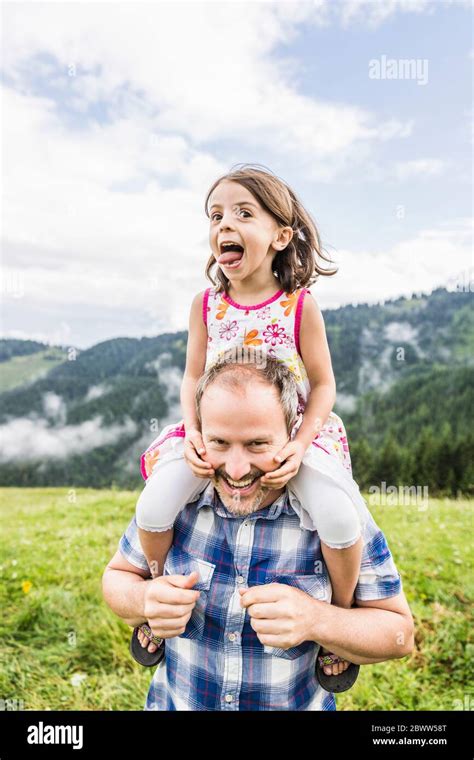 Happy Father Carrying Daughter On Shoulders On A Meadow In The