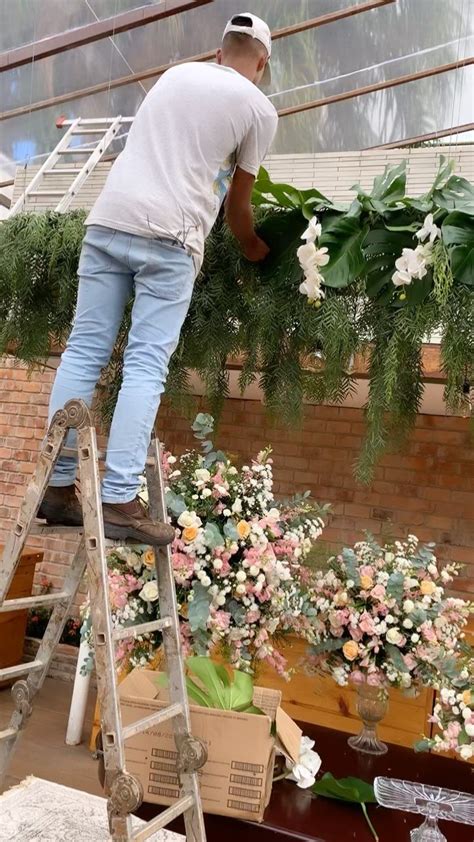 A Man Standing On A Ladder Next To A Bunch Of Flowers In A Room Filled