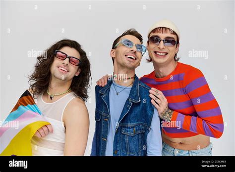 Three Appealing Jolly Gay Men With Stylish Sunglasses Posing With Rainbow Flag And Looking Away