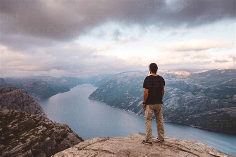 Man Standing At Edge Of Cliff At Preikestolen Norway Stock Photo