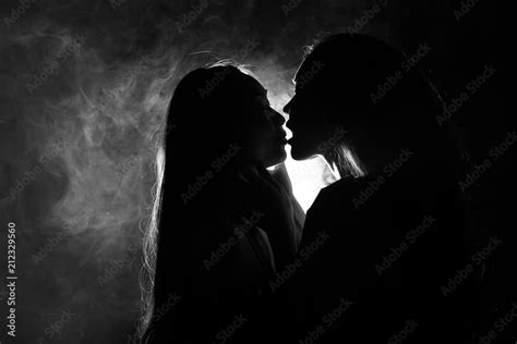 Silhouette Of Two Sexy Woman Kissing Holding In Darkness Through Light And Smoke ภาพถ่ายสต็อก