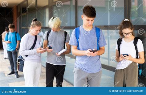 Students Look At The Screens Of Their Smartphones On City Street Stock