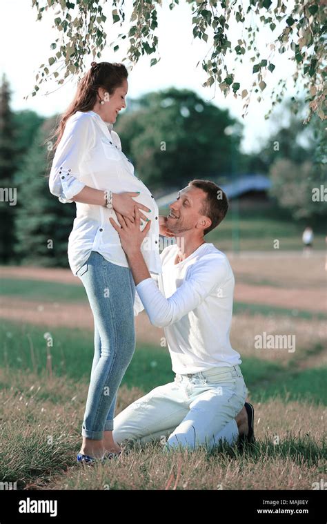 Happy Husband Embracing His Pregnant Wife On A Walk In The Park Stock