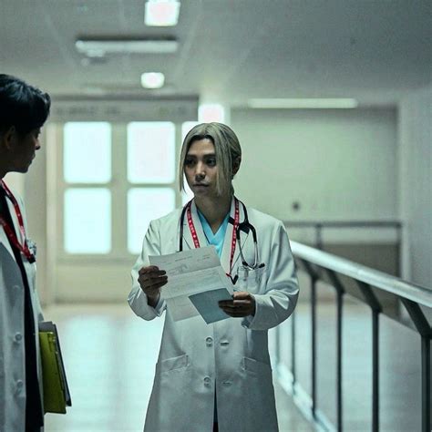 Two Doctors Standing In A Hallway Looking At Something On The Paper