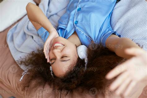 Joyful Curly Mulatto Lady Lying On The Bed With Her Head Down And Closed Eyes Dreaming And