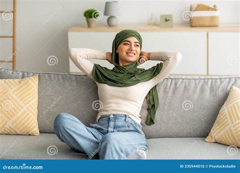 Beautiful Young Arab Woman In Hijab Sitting On Sofa With Hands Behind