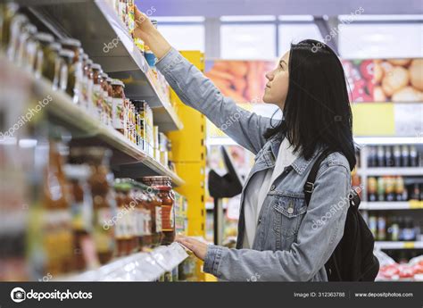 Красивая девушка выбирает товары на полках продуктового супермаркета ...