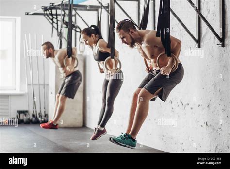 Three Attractive Young Male And Female Adults Doing Pull Ups On Rings