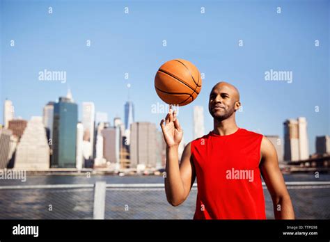 Smiling Man Spinning Basketball On Finger Against City Skyline Stock