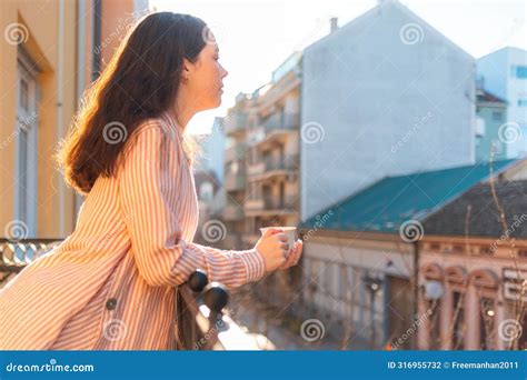 Side View Of Brunette Woman Drinks Her Morning Coffee Or Tea While Standing On Balcony There Is