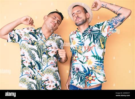 Jeune gay couple de deux hommes portant un chapeau d été et une chemise hawaïenne s étirant vers