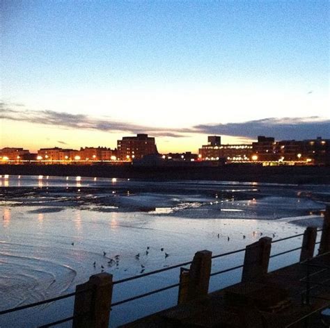 The Sun Is Setting Over An Icy Lake With Chairs On It And Buildings In