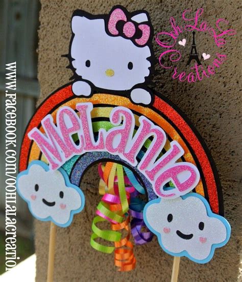 a hello kitty birthday cake topper on a stick with rainbows and clouds in the background