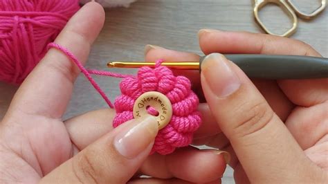 Someone Crocheting A Pink Flower With A Yellow Pin In Their Left Hand