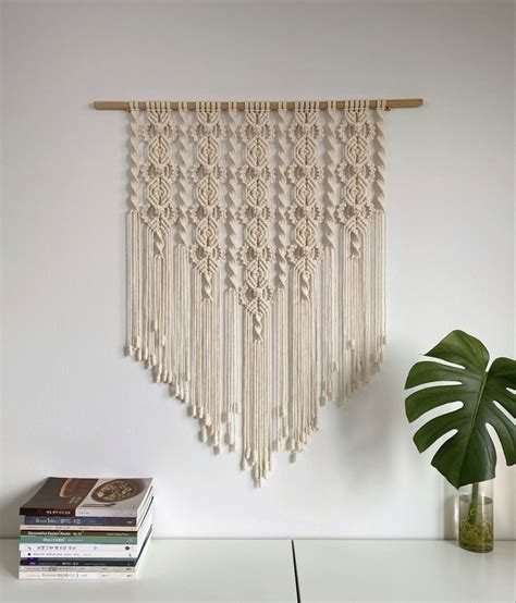 A Wall Hanging Made With Macrame And Tassels On A Shelf Next To A