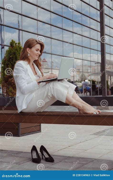 Barefoot Businesswoman In White Suit Sitting On Bench With Laptop