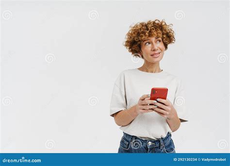 Ginger Curly Woman Wearing T Shirt Smiling And Using Cellphone Stock