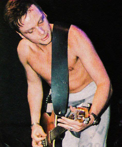 A Shirtless Man Holding An Electric Guitar In His Right Hand And