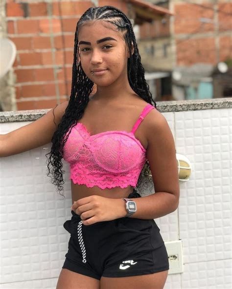 A Woman In Pink Bra Top And Black Shorts Standing Next To A White Brick