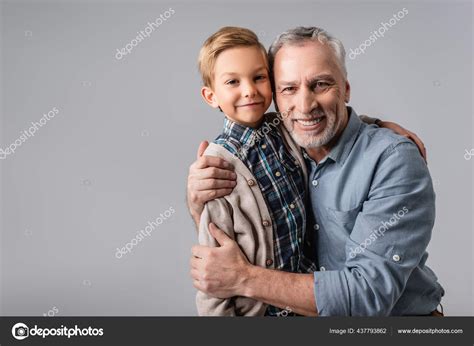 Happy Mature Man Embracing Smiling Grandson While Looking Camera