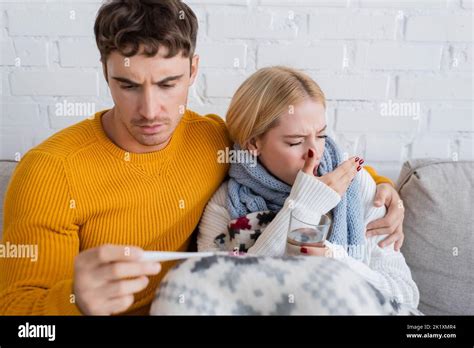 Man Holding Digital Thermometer And Hugging Sick Blonde Woman With
