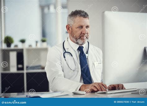 Connected To All Things In Healthcare A Mature Doctor Using A Computer At A Desk In His Office