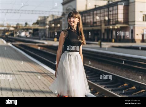 Female Brunette Traveler With Red Suitcase In White Skirt Waiting For A