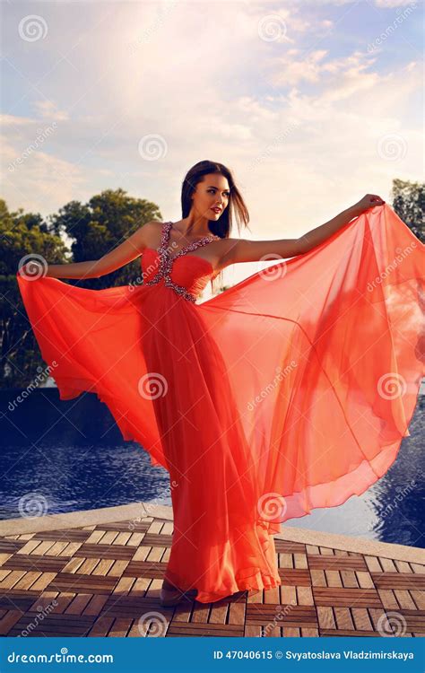 Beautiful Woman In Luxurious Red Dress Posing Beside A Swimming Pool