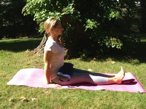 A Woman Sitting On Top Of A Pink Mat In The Middle Of A Park Doing Yoga