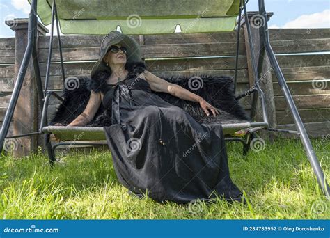 Portrait Of A Happy Elderly Woman 65 70 Years Old In A Straw Hat Resting On A Swing In The