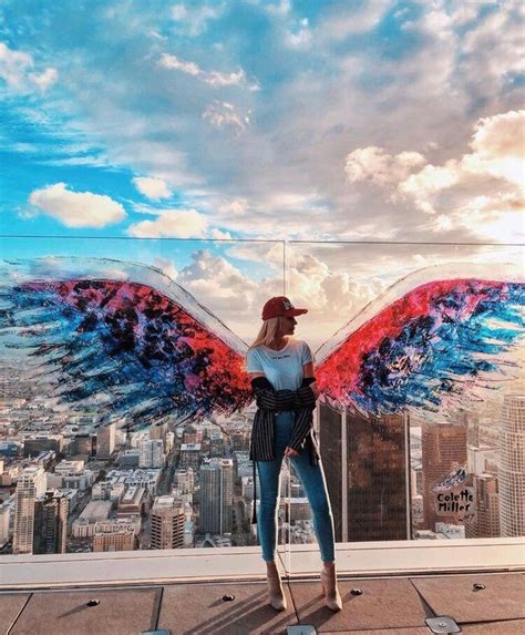 A Woman Standing On Top Of A Building With Wings Painted On The Side Of It