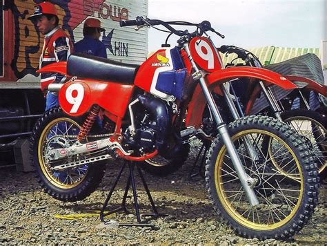 Two Dirt Bikes Parked Next To Each Other In Front Of A Truck With Men