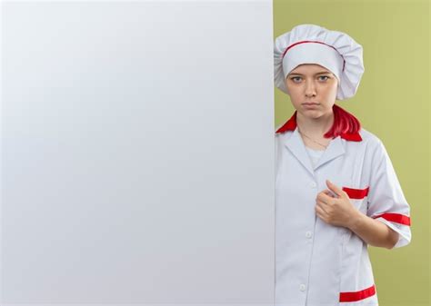 Jeune Femme Blonde Confiante Chef En Uniforme De Chef Se Tient Derrière Un Mur Blanc Et Semble
