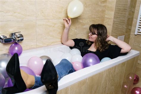 Young Woman Sitting In A Bathtub Full Of Balloons In Bathroom Stock