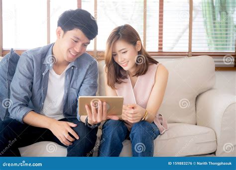 Asian Young Couple Relax Looking Tablet Entertainment On Internet Together On Sofa At Home Stock