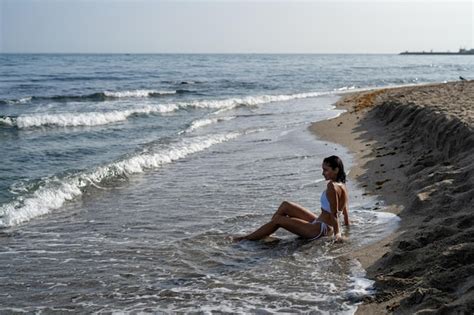 Premium Photo Beautiful Brunette Girl In A White Swimsuit Sits On The Sand On The Seashore