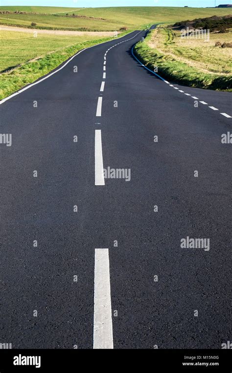 A Grey Asphalt Country Road With Strong White Lines In The Middle The