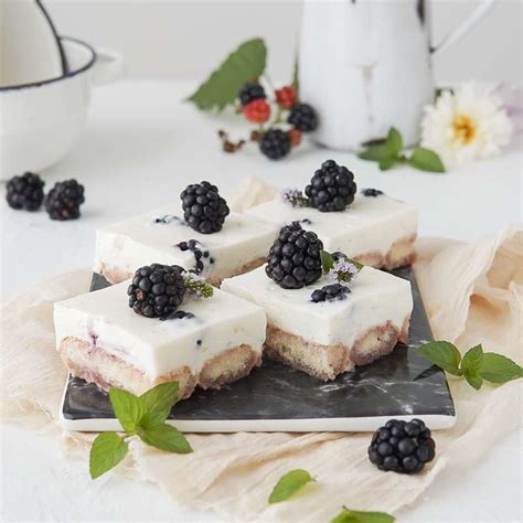 Four Pieces Of Cake On A Plate With Blackberries And Mint Leaves Around