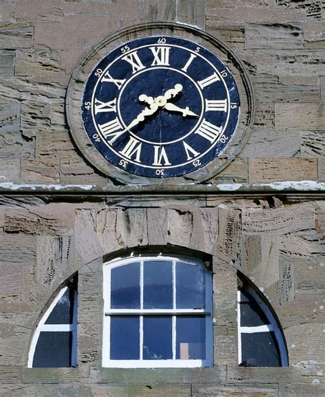 A Large Clock Mounted To The Side Of A Brick Building With Roman Numerals