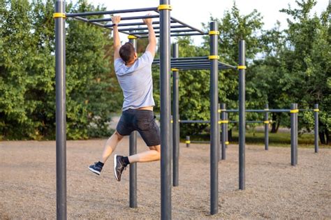 A Man Trains In An Open Area And Pulls Himself Up On A Horizontal Bar