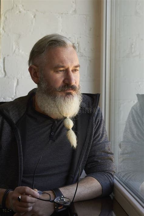 Half Length Portrait Of Mature Gray Haired Man With Original Beard On Window Background