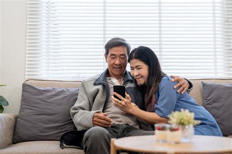 Happy Elderly Asian Couple Using Smartphone Sit On Sofa Doing Ecommerce Shopping Online On