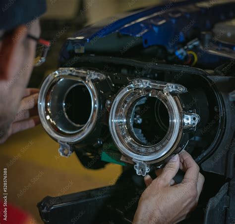 Car headlight in repair close-up. The car mechanic installs the lens in the headlight housing ...