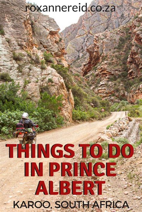 A Man Riding A Motorcycle Down A Dirt Road Next To A Mountain Covered