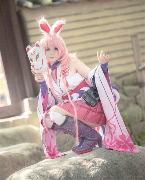 A Woman With Pink Hair And Bunny Ears Is Sitting On A Rock Holding A Mask