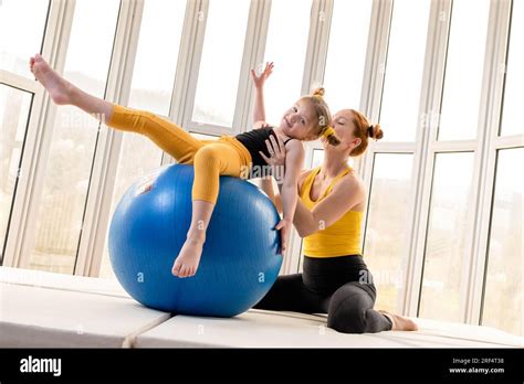 Young Fit Mom And Her Daughter Having Fun With Fitness Ball In A Gym