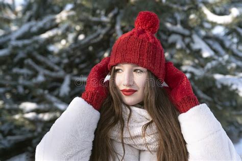 Beautiful Young Girl Straightens Hat In Winter Park Against Snowy Pine