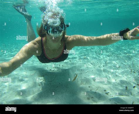 Female Swimmer Wearing Mask And Fins Blowing Air Bubbles Underwater In Ocean Over Sandy Bottom