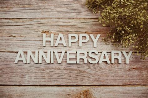 Happy Anniversary alphabet letters with flowers frame on wooden background.