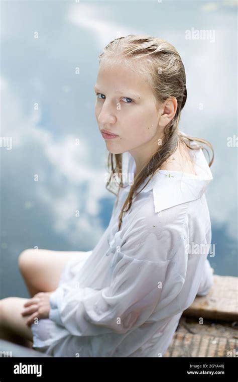 Blonde Teenage Girl In White Wet Shirt Is Sitting By The Blue Water